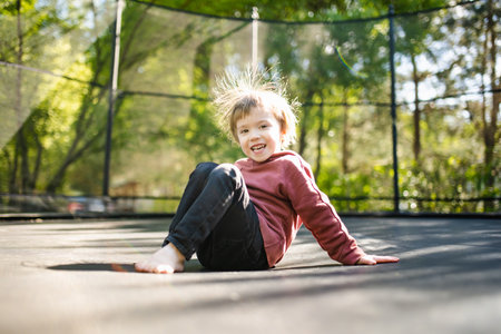 Cute little boy jumping on a trampoline in a backyard on warm and sunny summer day. Sports and exercises for children. Summer outdoor leisure activities.の写真素材