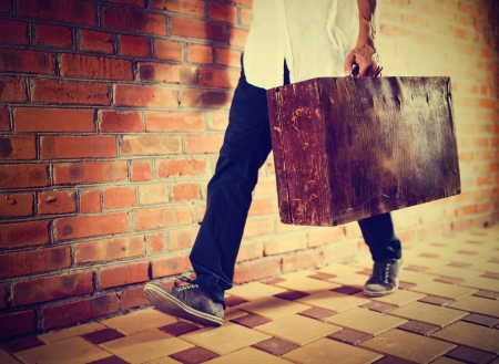 Young man walking along street with old suitcase, retro tintedの写真素材