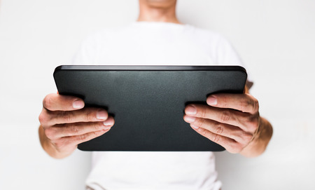 Man in white t-shirt using tablet pc, white wall on background の写真素材