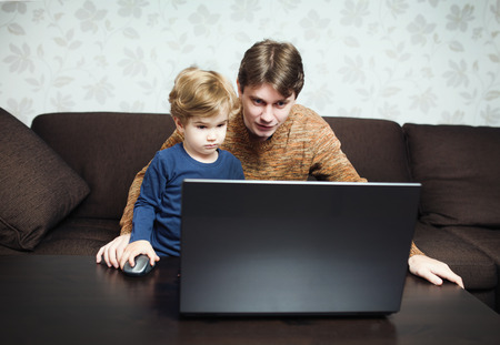 Father and son using laptop on sofa in houseの写真素材