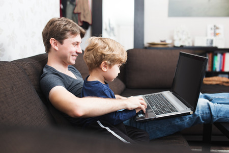 Father and son using laptop on sofa in houseの写真素材