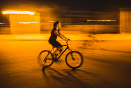 Happy bicyclists riding bikes in a city after sunset, motion blurの写真素材