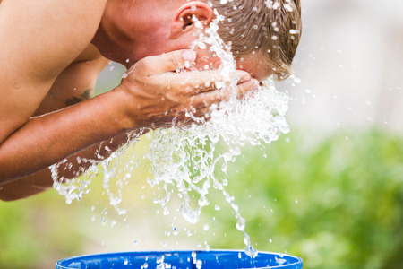 A man refreshes himself with a splash of cool, fresh water on his face.の写真素材
