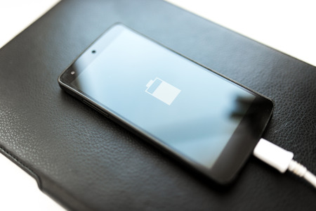 Close-up of smartphone with low battery symbol on chargeの写真素材