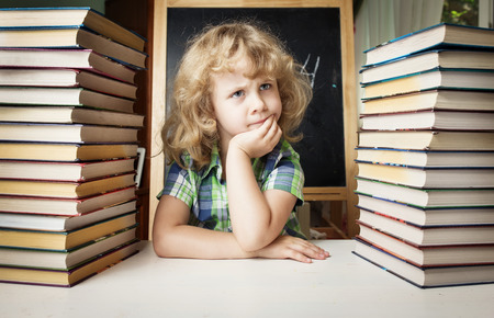 Portrait of cute schoolgirl thinking while sitting with stack of books at table, education conceptの写真素材
