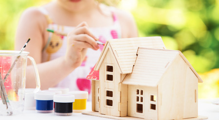 Llittle girl paints wooden model of house,  summer outdoor, new home conceptの写真素材