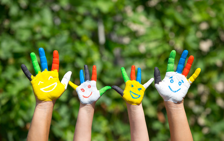 Colored hands with smile painted in colorful paints against green summer background. Lifestyle conceptの写真素材