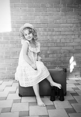Girl sitting on a suitcase with binoculars. Travel concept. Black and white photoの写真素材