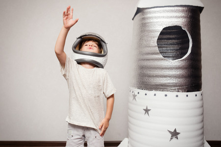 Happy child dressed in an astronaut costume playing with hand made rocket.
