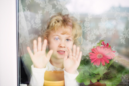 Adorable little girl looking through the windowの写真素材