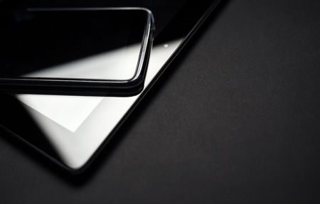 Smartphone Leaning On Tablet close up photo. Electronic devices on black background.の写真素材