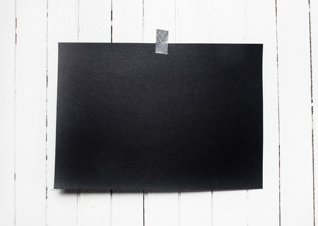 Blank black poster hanging on a tape on white wooden plank wall. Template background for your...