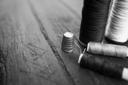 Sewing accessories: bobbins of thread, scissors, thimble on wooden table. Black and white photo. Tailoring and sewing concept.の写真素材