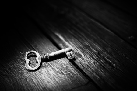 Rusty key on old wooden surface, black and white photo.の写真素材