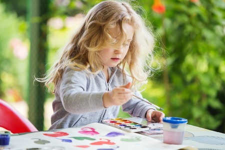 Portrait of little blonde girl painting, summer outdoor.の写真素材
