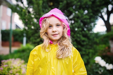 Outdoor photo of little blonde girl in yellow raincoat.の写真素材