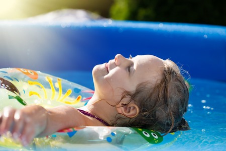 Portrait of cute little girl in blue big inflatable pool outdoors.の写真素材