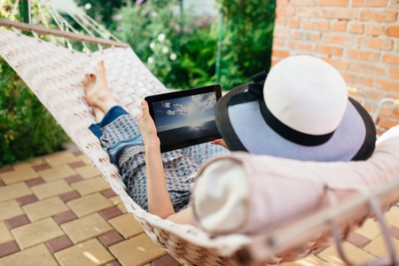 Woman using tablet computer while relaxing in a hammock.の写真素材