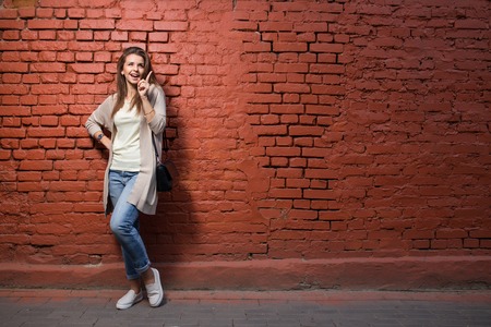 Young beautiful happy woman in casual cloths against red brick wallの写真素材