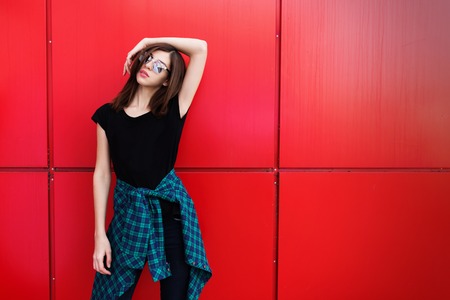 Portrait of girl in rock black style, standing outdoors in the city against the red urban wall.