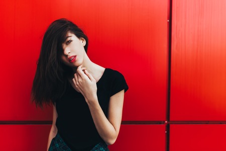 Portrait of girl in rock black style, standing outdoors in the city against the red urban wall.の写真素材