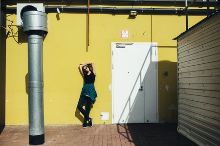 Brunette girl in rock black style, standing against yellow wall outdoors in the city street.の写真素材