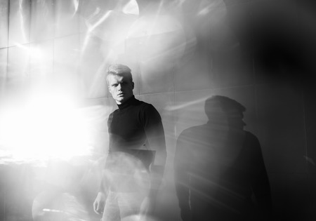 Black and white artistic photography. Young blonde man in black wear standing on street.の写真素材