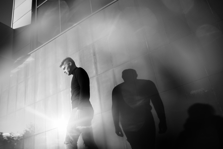 Black and white artistic photography. Young blonde man in black wear standing on street.