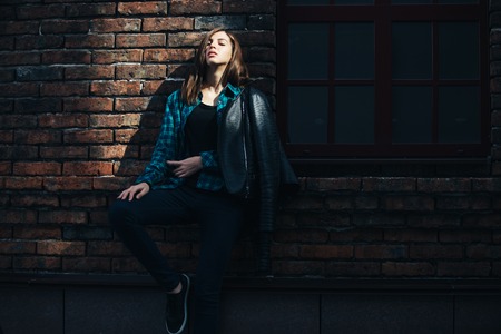 Lifestyle fashion portrait of brunette girl in rock black style, standing outdoors in the city street.の写真素材