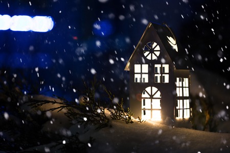 Lantern house with burning candle on snow in the evening.