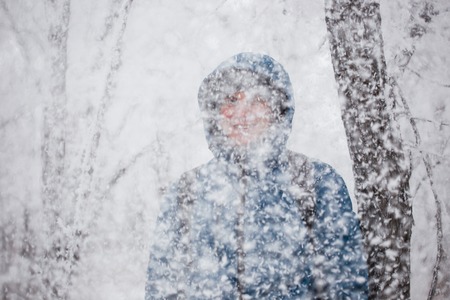 Young handsome man standing in snowfall on background of snowy forest.の写真素材