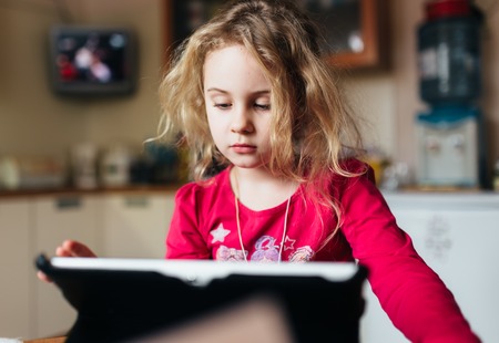 Blonde child girl using tablet computer at home