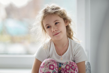Portrait of cute blonde child girl sitting near windowの写真素材