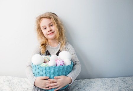 Little blonde girl holding basket with painted eggs. Easter day.の写真素材