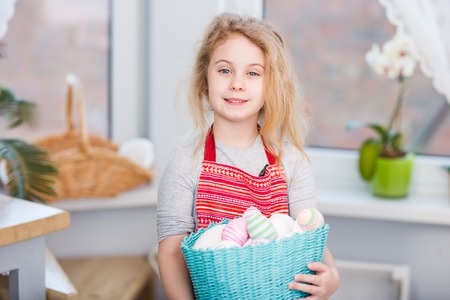 Little blonde girl holding basket with painted eggs. Easter day.の写真素材