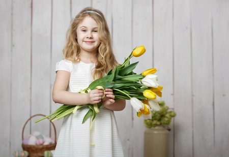 Portrait of cheerful little blonde girl with tulips bouquet on white wood backgroundの写真素材