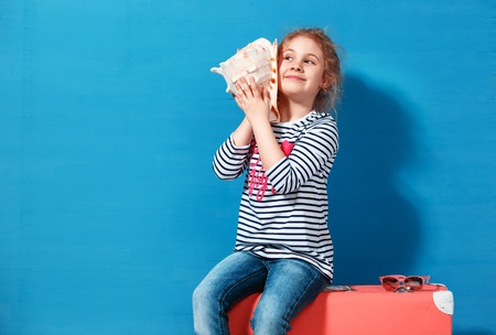 Portrait of blonde child girl listen a seashell at the blue wall. Summer vacation conceptの写真素材