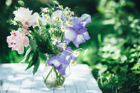 Bouquet of white peonies, chamomiles and iris flowers in glass vase. Summer background. Tinted photoの写真素材