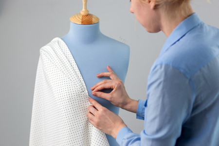 Seamstress measuring beautiful fabric on blue tailor dummy in her workshopの写真素材