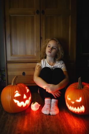 6 year old girl sitting on the floor with two scary halloween pumpkins at night.の写真素材