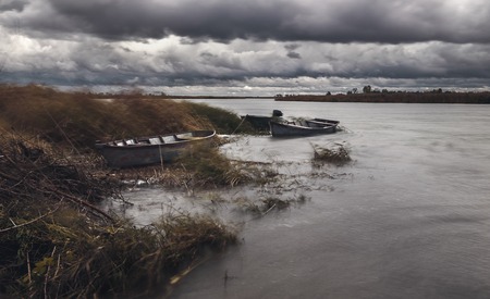 Storm clouds over river bank with wooden boats at autumn day.の写真素材