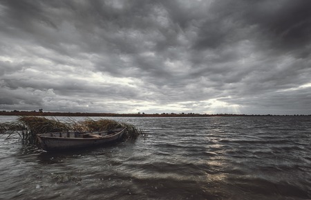Storm clouds over river bank with wooden boat at autumn dayの写真素材