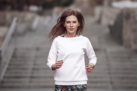 Young sporty girl jogging in city park at autumn day.の写真素材