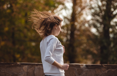 Young sporty girl jogging in city park at autumn day.の写真素材