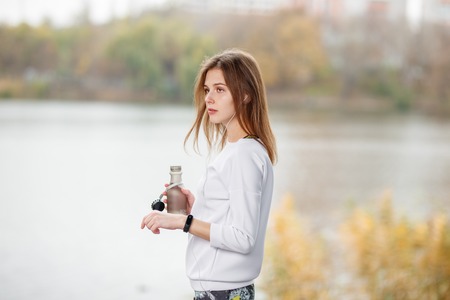 Young fitness girl with bottle of water standing outdoor in city park.の写真素材