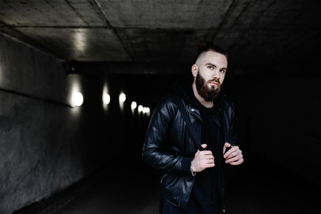 Modern young bearded man in black style clothes standing in around urban background.の写真素材