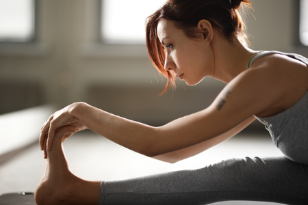 Young sporty woman doing yoga stretching exercise sitting in gym near bright windowsの写真素材