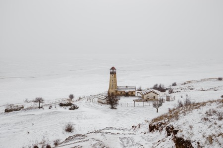 Old wooden lighthouse at edge of frozen harbor with cloudy skyの写真素材