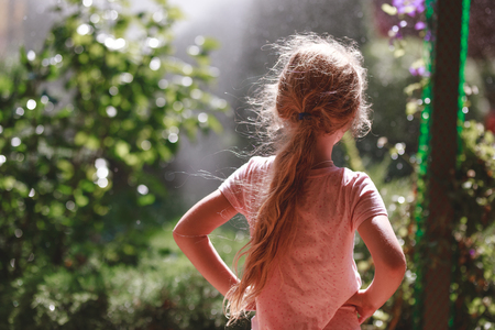 Back view of seven years old blonde girl wearing pyjamas standing outdoor in home garden in the early morningの写真素材
