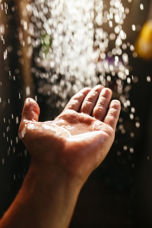 A mans hand in a spray of water in the sunlight against a dark background. Water as a symbol of purity and lifeの写真素材